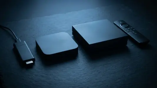 Four streaming devices and a remote control arranged on dark slate, lit with cool blue light
